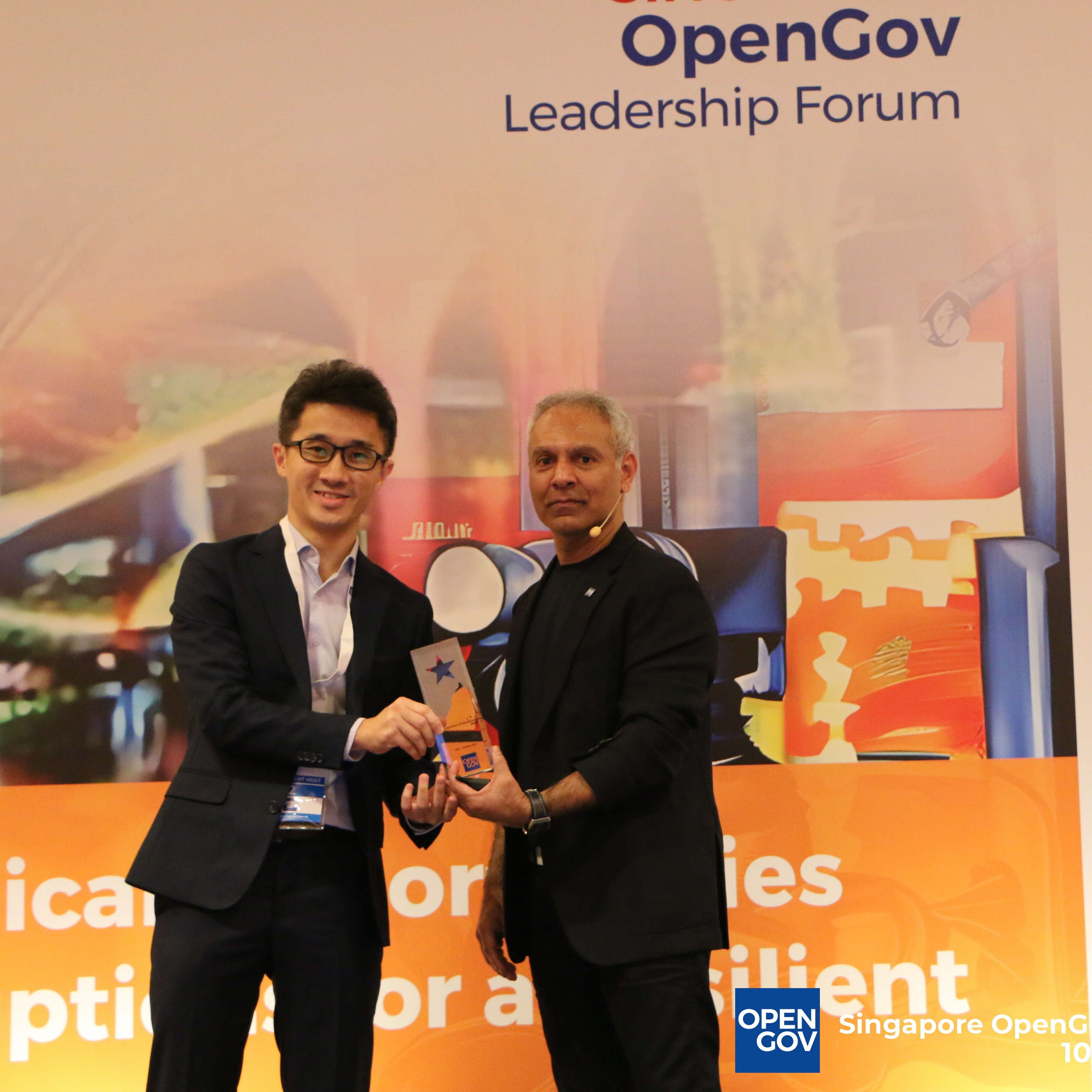 Two men hold a trophy together on stage at the OpenGov Leadership Forum in Singapore.